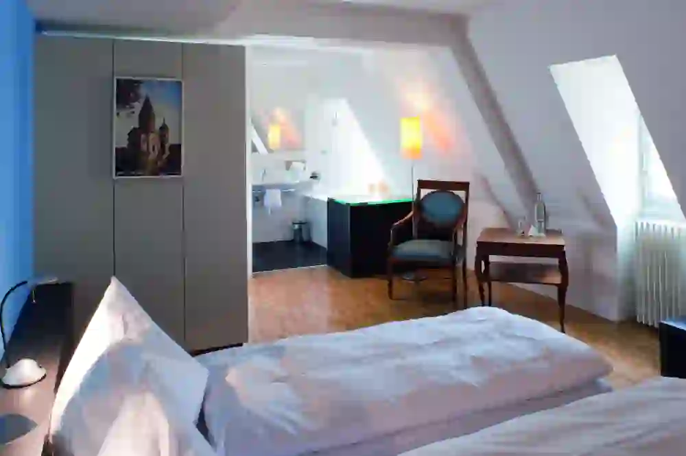 L'immagine mostra un'accogliente camera per gli ospiti del Castello di Münchenwiler, arredata con stile. La luce calda e i colori tenui creano un'atmosfera rilassante e invitante, ideale per rilassarsi in un ambiente storico.