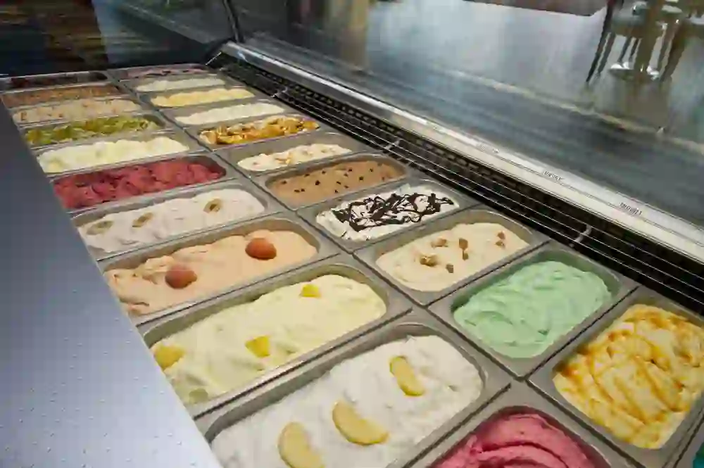 Una varietà di gusti di gelato in un banco della Gelateria Riva crea un'immagine di seduzione e scelta, pronta a soddisfare ogni gusto e a far sorridere gli astanti.