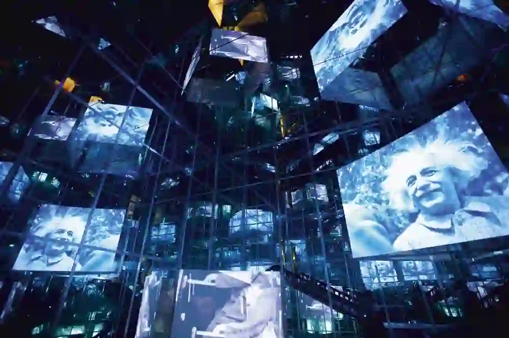 The picture shows an impressive, modern exhibition installation in the Bernisches Historisches Museum, which creates a fascinating, almost floating atmosphere with a multitude of floating screens showing iconic images of Albert Einstein.