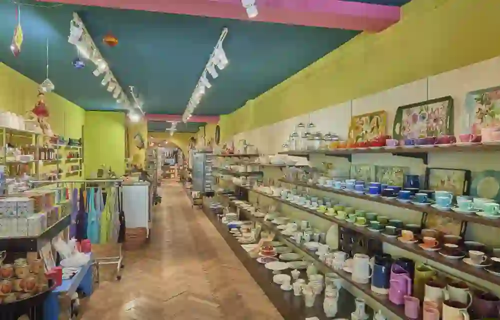 The picture shows the colourful and lovingly designed interior of Iljos Cucina. Shelves full of colourful cups, bowls and kitchen accessories line the walls. Warm colours, decorative details and the wooden herringbone parquet flooring give the shop an inviting, charming atmosphere - a place that invites you to browse and discover.
