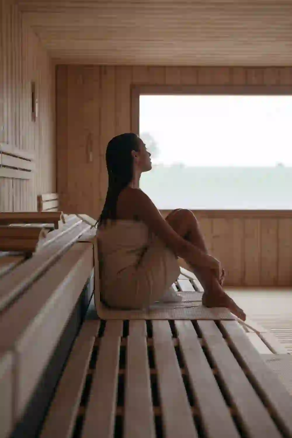 A woman sits deeply relaxed in the wood-panelled sauna at the Solbad & Spa Schönbühl, gazing thoughtfully into the distance and enjoying the soothing silence.