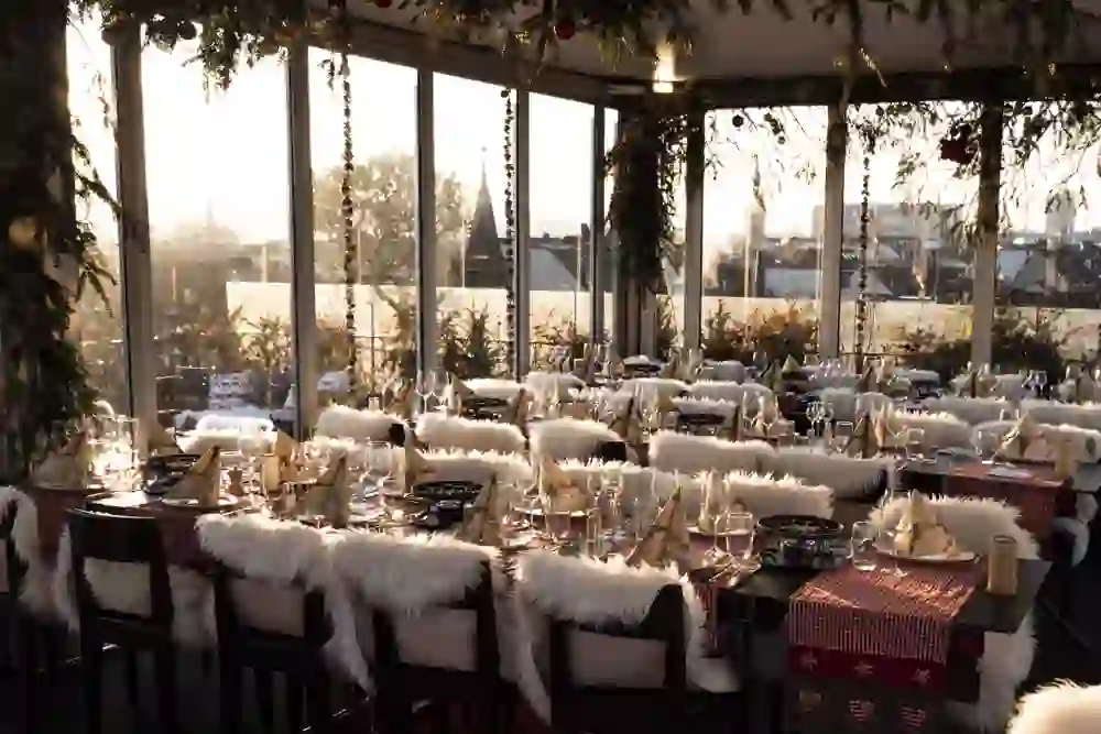 Das Bild zeigt ein festlich dekoriertes Restaurant auf einem Dach, mit langen Tischen, roten Tischdecken und weichen, weißen Pelzdecken auf den Stühlen. Die Atmosphäre ist gemütlich und elegant, mit warmem Licht, das eine einladende Stimmung schafft.