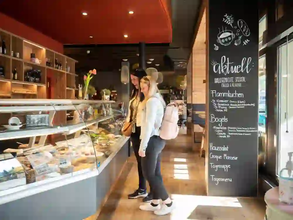 Zwei Frauen schauen sich mit einem Lächeln die Auswahl im gemüstlichen Bistro B5 in Burgdorf an. Die warme Inneneinrichtung und die fröhliche Atmosphäre laden zum Verweilen und Geniessen der frischen, regionalen Angebote ein.