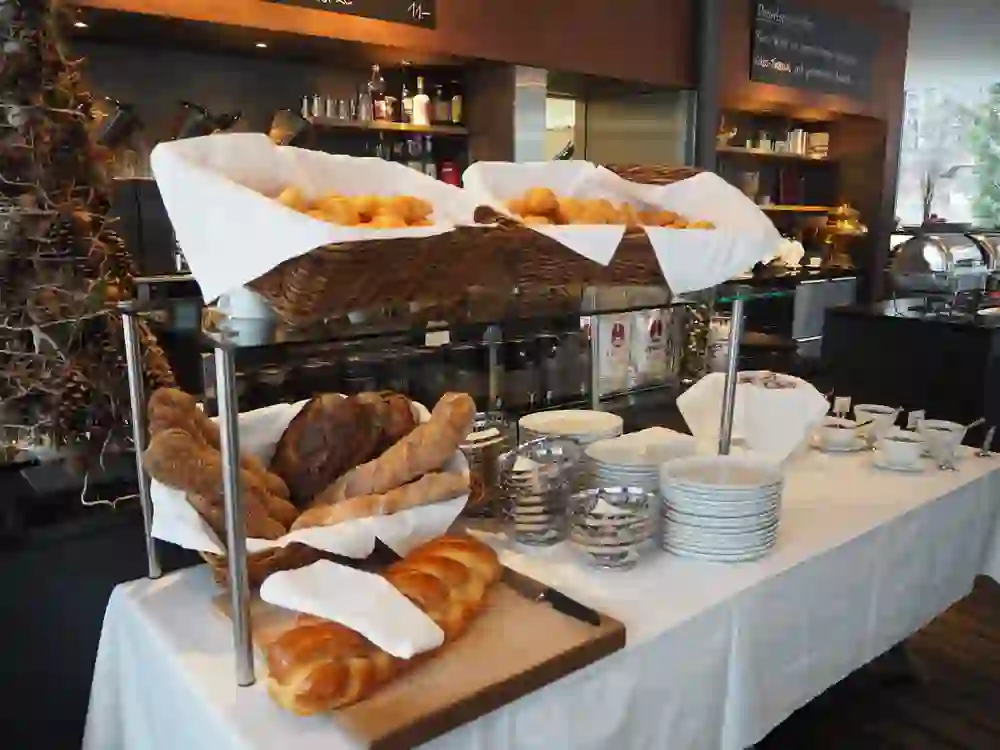 Das Bild zeigt einen Brunch-Buffettisch im Restaurant Schwellenmätteli in Bern mit Körben voller Croissants, verschiedenen Brotarten, Tellerstapeln und Schalen für Essen, sowie Getränkespendern im Hintergrund.