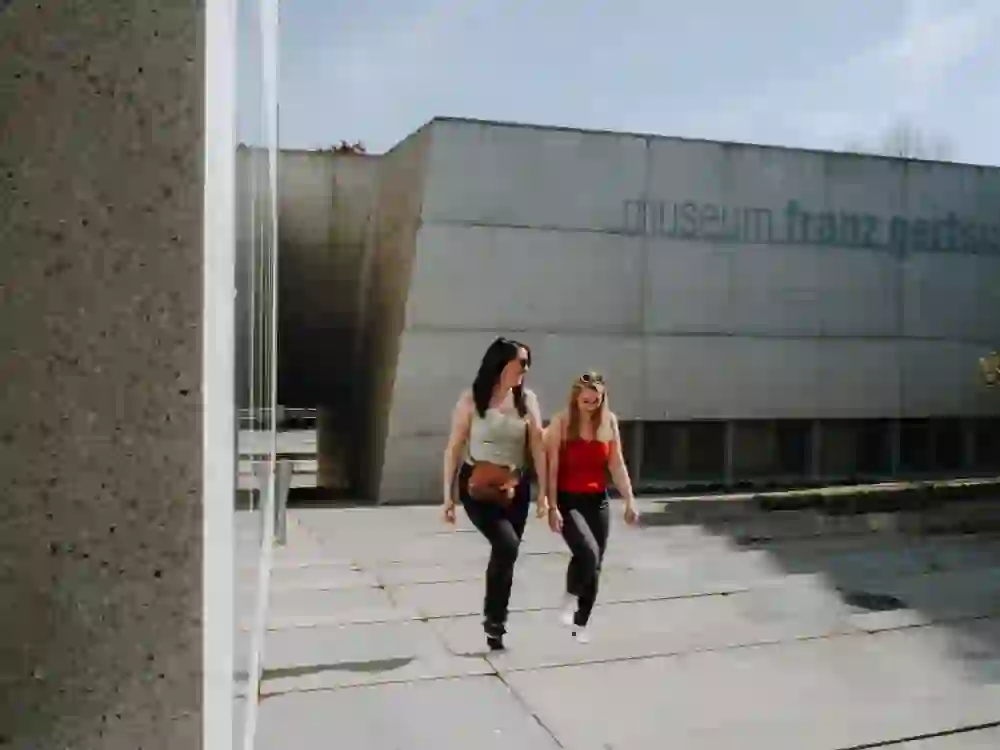 Due donne passeggiano davanti al Museo Franz Gertsch di Burgdorf, rilassate e impegnate in una conversazione, la cui architettura moderna costituisce un interessante contrasto con il vivace dialogo tra i visitatori.