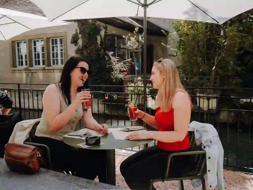 An einem sonnigen Tag geniessen zwei Freundinnen entspannt ihre Getränke auf der Terrasse im Stadtcafé in Burgdorf. Ihre fröhlichen Gesichter und das angeregte Gespräch spiegeln die Leichtigkeit des Moments wider.