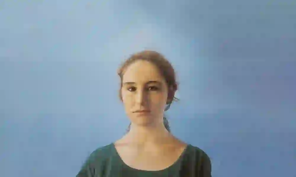 Das Bild zeigt ein Porträt einer jungen Frau vor einem sanften blauen Hintergrund. Ihr Blick ist nachdenklich und ruhig, vermittelt eine tiefe Innenschau und eine stille, introspektive Stimmung.