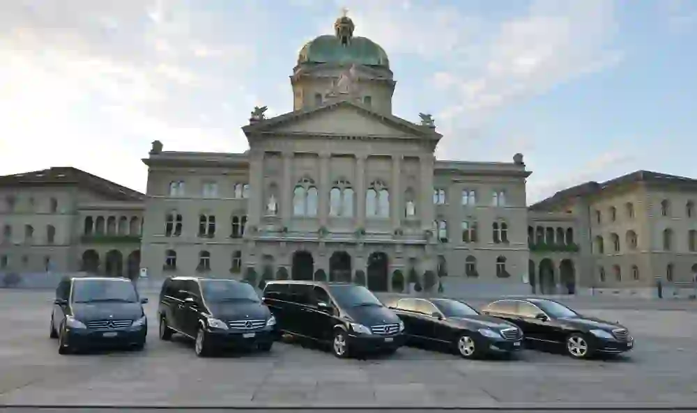 Eine Flotte von schwarzen Limousinen steht bereit vor dem prachtvollen Bundeshaus in Bern, was auf eine bevorstehende wichtige Veranstaltung oder Ankunft von VIPs hindeutet und eine Atmosphäre formeller Erwartung schafft.