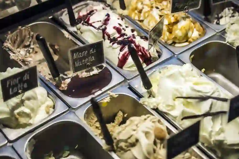 Una colorata selezione di gusti di gelato è esposta in una gelateria. I colori ricchi e le insegne con nomi come "Mare di Nutella" risvegliano il desiderio e suggeriscono un momento di piacere e varietà.
