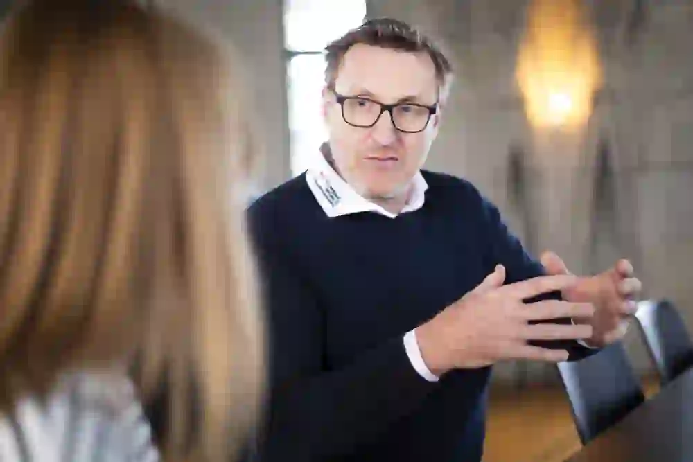 Martin Ryhner en conversation montre sa passion par des gestes engagés ; son regard concentré révèle un intérêt profond pour le sujet. L'atmosphère est marquée par une discussion sérieuse mais ouverte.
