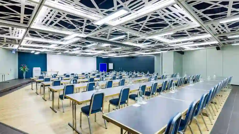 Das Bild präsentiert den Raum Honegger und Gnägi im Sorell Hotel Ador in Bern, einladend gestaltet für grosse Veranstaltungen. Die Anordnung der blauen Stühle in Reihen und die hellen Farben schaffen eine Atmosphäre der Aufmerksamkeit und Konzentration.