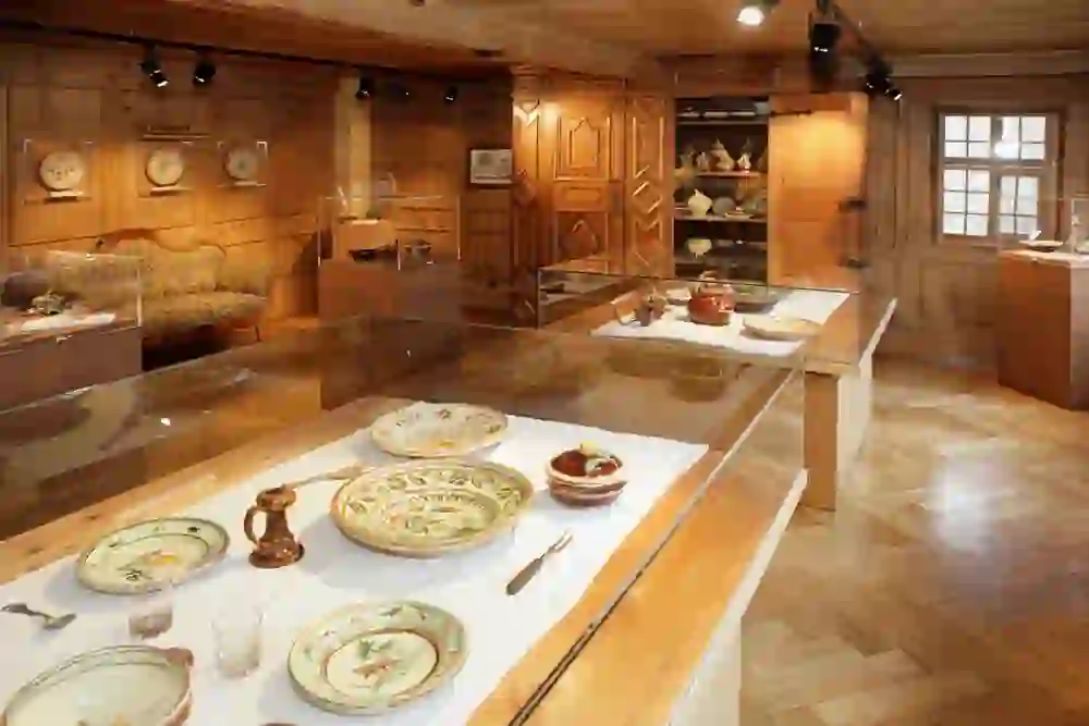 Ein behaglicher Ausstellungsraum im Regionalmuseum Chüechlihus in Langnau, gefüllt mit kunstvoll verziertem Geschirr und volkstümlichen Möbeln, strahlt Wärme und die Essenz ländlichen Lebens aus.