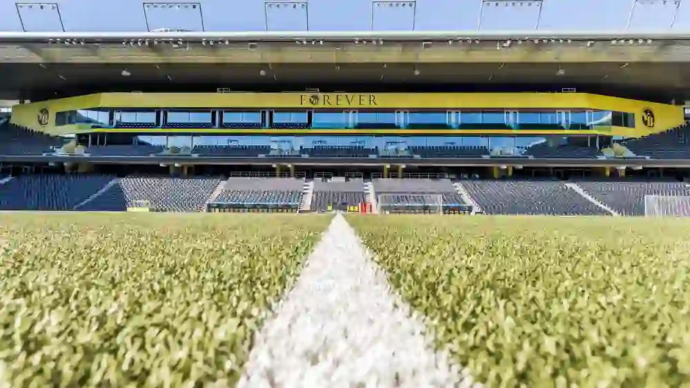 L'immagine offre la prospettiva di un campo da calcio nello stadio Wankdorf, con l'attenzione sulla linea di metà campo. Gli spalti sono vuoti e attendono i tifosi che porteranno energia e tifo. Un momento di silenzio in un'arena piena di ricordi.