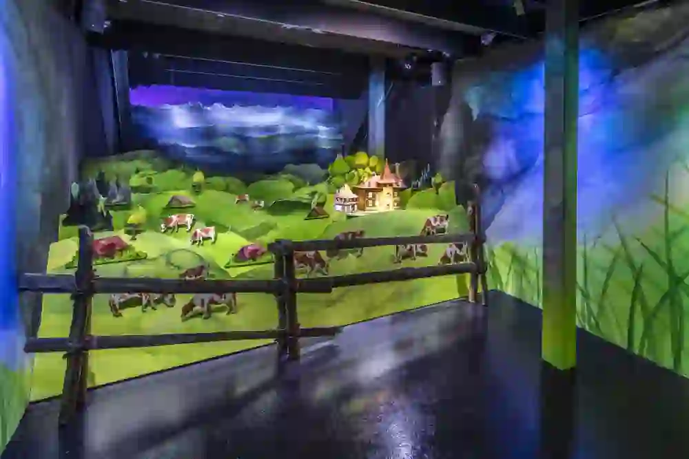 Das Bild entführt in eine verspielte Miniaturwelt des Emmentaler Königswegs, strahlend und einladend, wo farbenfrohe Landschaften und Kühe eine idyllische, fast märchenhafte Stimmung zaubern.