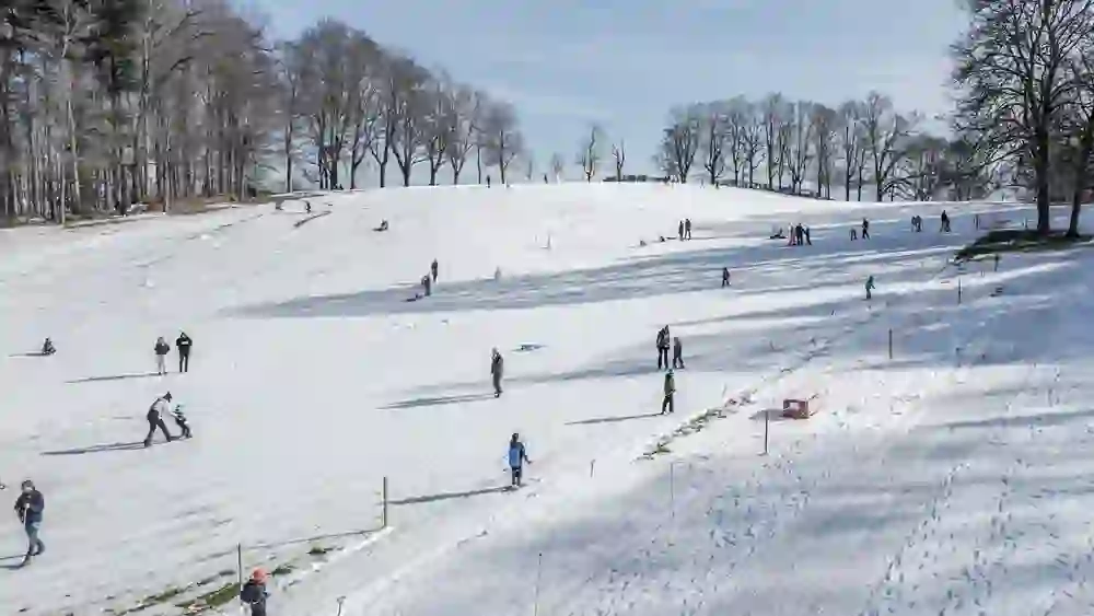 Sur la pente enneigée du Gurten, familles et enfants s'ébattent, certains font du ski ou de la luge, d'autres profitent du soleil hivernal. L'ambiance est joyeuse, détendue et remplie d'une joie hivernale vivante.