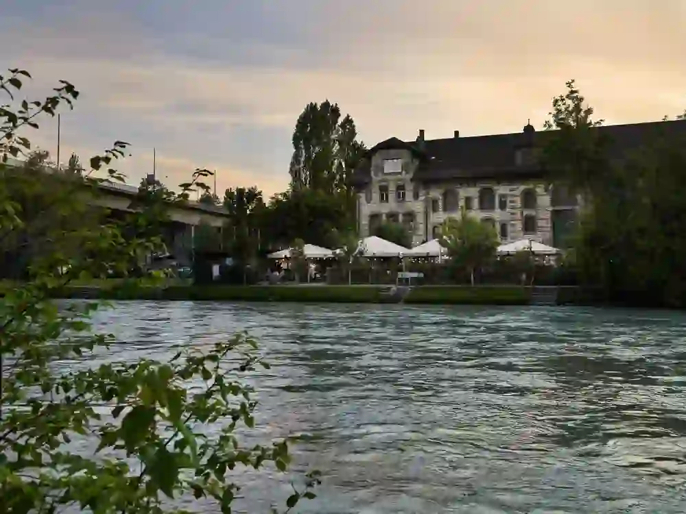 The picture shows the historic building on the banks of the lively River Aare at dusk, with the peaceful atmosphere and idyllic outdoor area of the Dampfzentrale restaurant inviting you to linger.