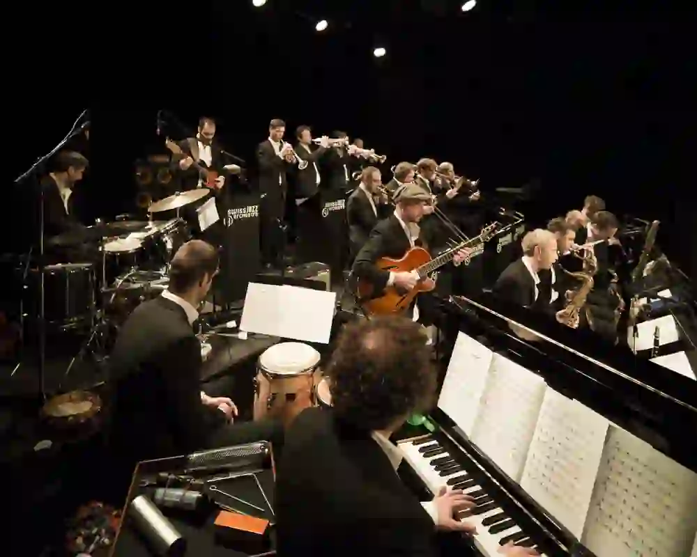 La scena dinamica di un concerto della Swiss Jazz Orchestra, con i musicisti in azione, incarna l'energia, l'armonia e la passione per la musica jazz.