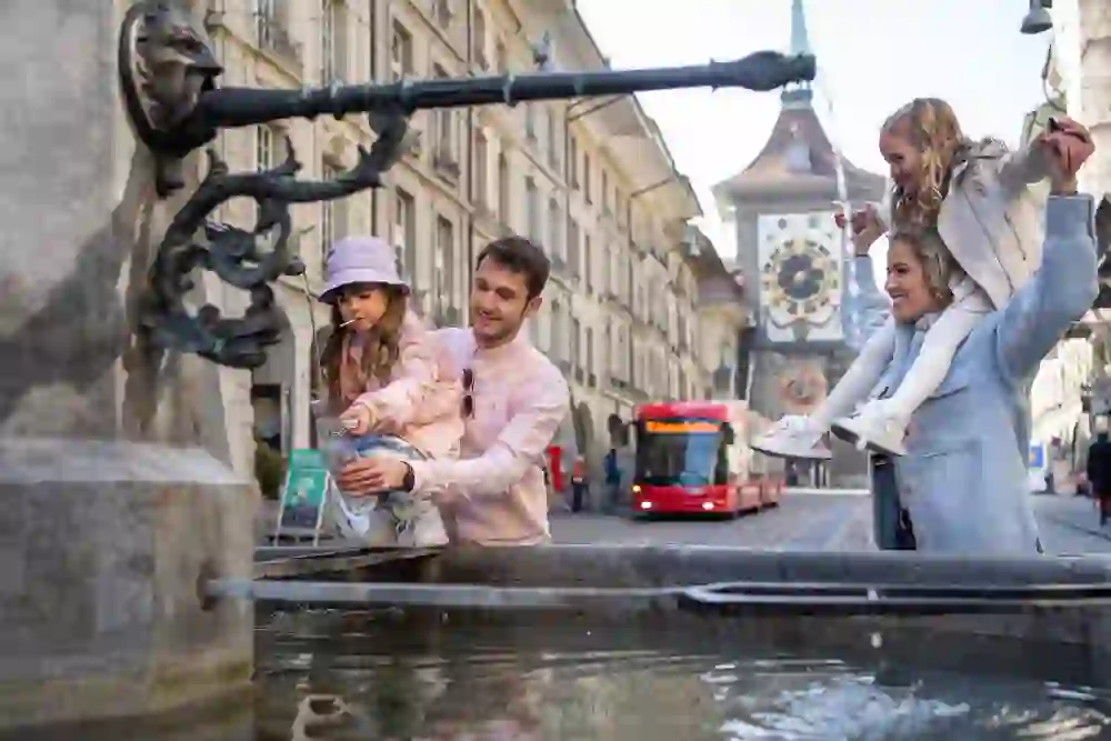Auf dem Bild ist eine Familie an einem Brunne vor der Zytglogge zu sehen.