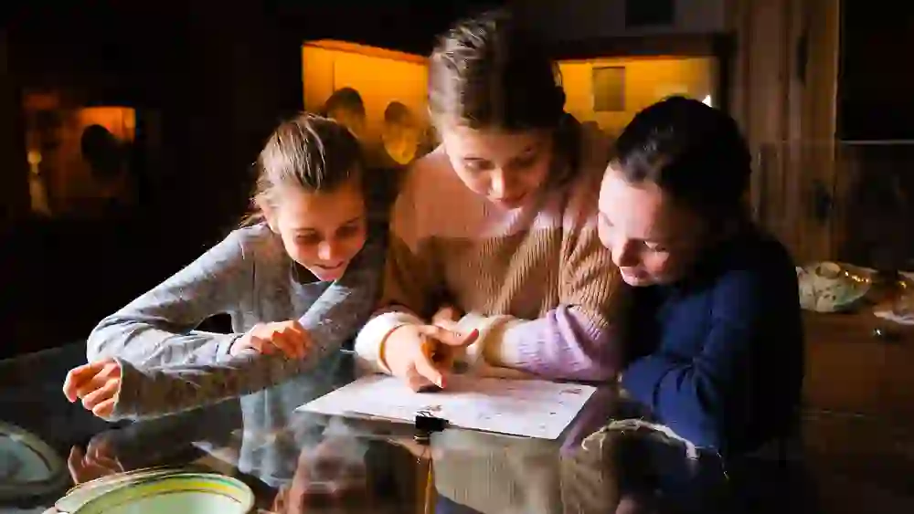 Im Regionalmuseum Chüechlihus in Langnau vertiefen sich drei junge Besucherinnen, beleuchtet vom warmen Schein der Ausstellung, gemeinsam in eine Lernaufgabe, umgeben von historischem Erbe.