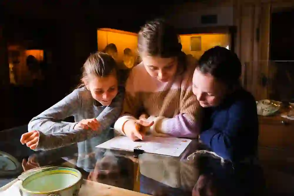 In the Chüechlihus regional museum in Langnau, three young visitors, illuminated by the warm glow of the exhibition, immerse themselves in a learning task together, surrounded by historical heritage.