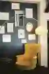 The picture shows a cosy café corner with a yellow armchair and a stylish floor lamp, surrounded by works of art that create a creative and relaxed atmosphere.