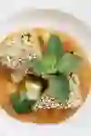 Una zuppa appetitosa, servita con pane al sesamo e guarnita con menta fresca, presentata su un piatto bianco, invita a gustare uno spuntino fresco e aromatico.