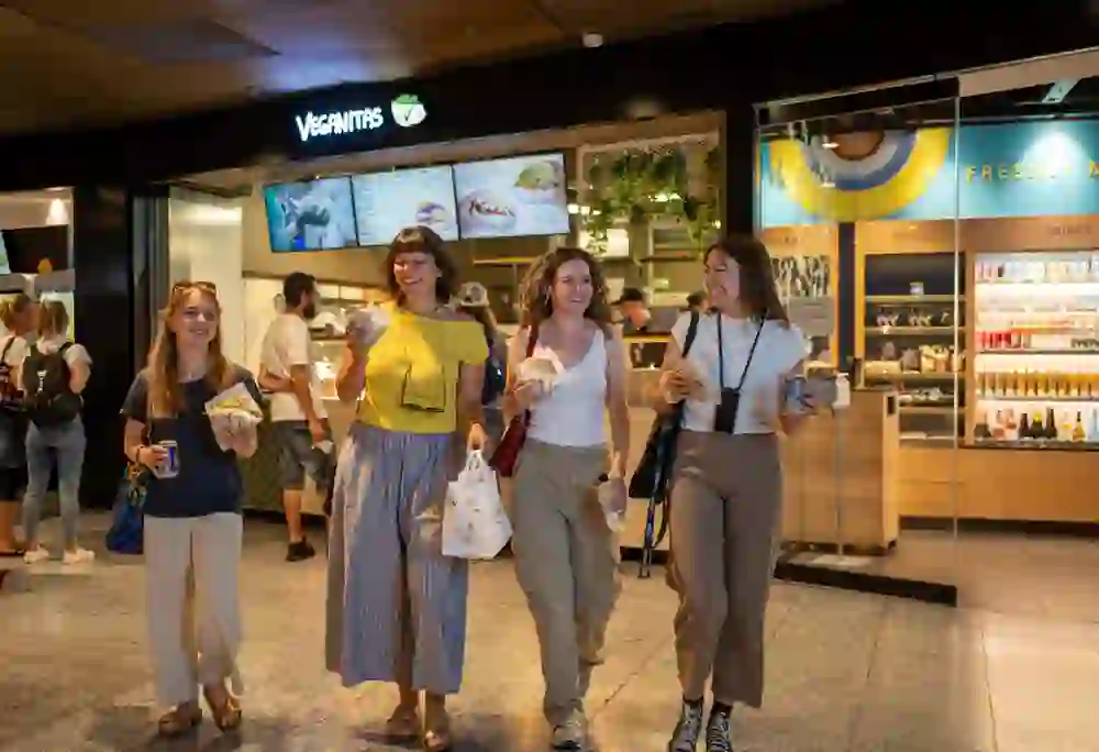 Vier Frauen laufen mit gefüllten Pitas in der Hand vom Restaurant Veganitas fort. Sie lachen und das Bild strahlt Freude aus.