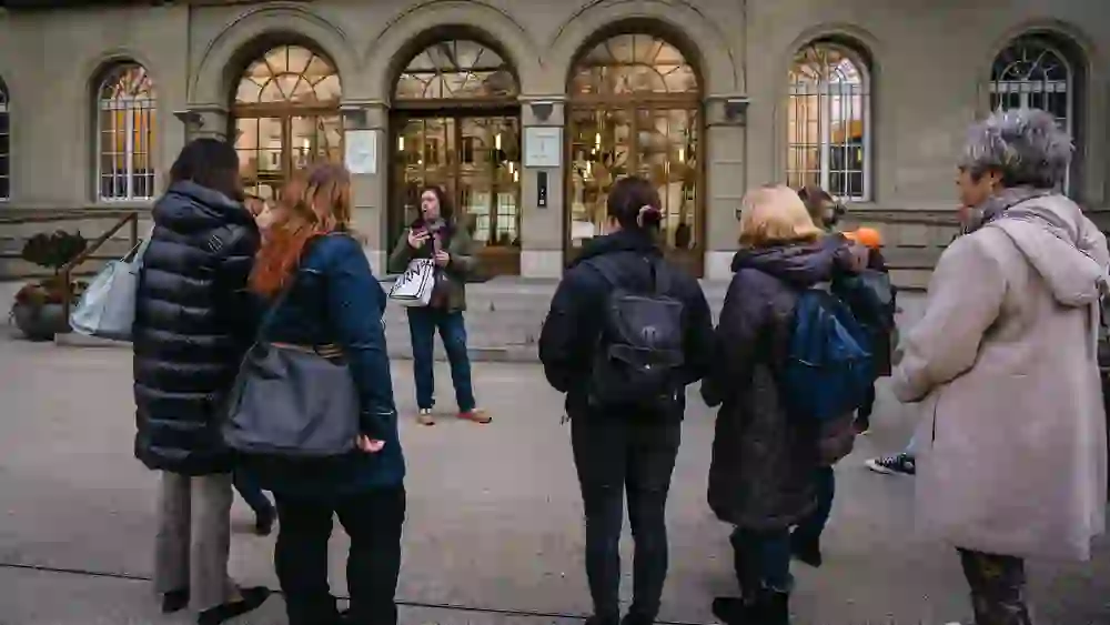 Eine aufmerksame Gruppe hört einem Stadtführer zu, der vor einem historischen Gebäude in Bern steht. Die Teilnehmer wirken interessiert und eingehüllt in warme Jacken, was auf eine lehrreiche und gemütliche Atmosphäre während der „1848 – Bern wird Bundesstadt“ Tour hindeutet.