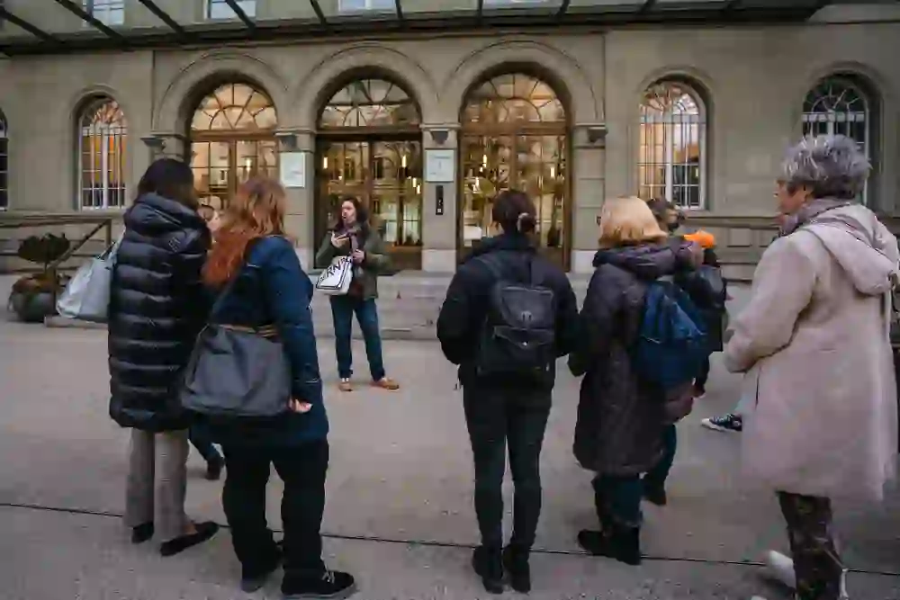 Eine aufmerksame Gruppe hört einem Stadtführer zu, der vor einem historischen Gebäude in Bern steht. Die Teilnehmer wirken interessiert und eingehüllt in warme Jacken, was auf eine lehrreiche und gemütliche Atmosphäre während der „1848 – Bern wird Bundesstadt“ Tour hindeutet.