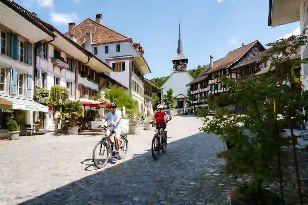 Zwei Radfahrer erkunden die charmante, sonnendurchflutete Altstadt auf der Zeitschlaufe Laupen, umgeben von traditioneller Architektur und einem Gefühl von Frieden und historischem Flair.
