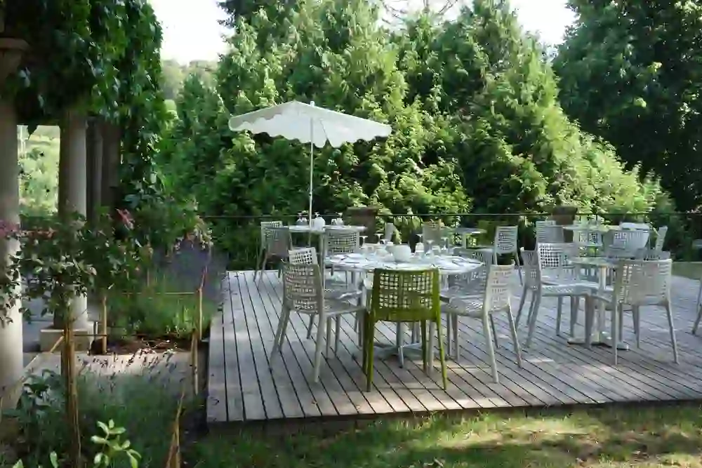 L'immagine mostra una tranquilla ed elegante terrazza all'aperto del Castello di Münchenwiler, circondata da una vegetazione lussureggiante e da piante fiorite. L'atmosfera rilassata invita ad assaporare momenti nella natura, perfetti per cenare all'aperto.