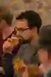 Das Bild zeigt einen Mann, der ein Glas Bier in der Hand hält und es sorgfältig betrachtet, vielleicht um Farbe, Klarheit und die Bläschen zu beurteilen. Seine Mimik deutet darauf hin, dass er sich auf den Geschmack und das Aroma konzentriert. Im Hintergrund sind weitere Personen zu erkennen, die ebenfalls Bierproben geniessen und an der Biertour teilnehmen. Die Umgebung erscheint gemütlich und von sanftem Licht erleuchtet.