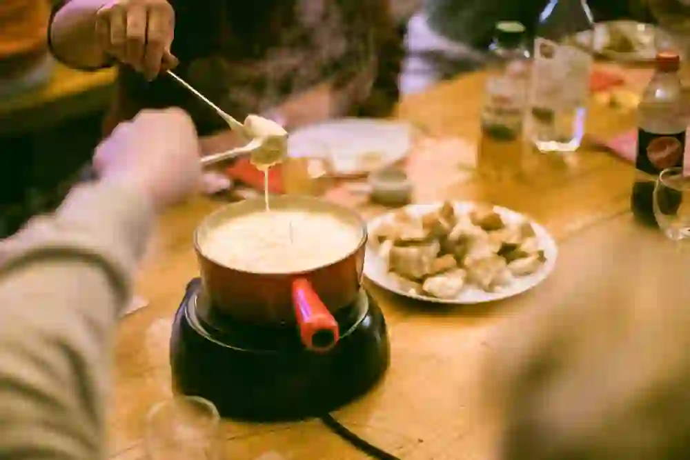 Das Bild zeigt ein gemütliches Fondue-Essen. Zwei Personen tauchen Brotstücke in den dampfenden Käse. Die warme, einladende Atmosphäre und die Freude am gemeinsamen Essen sind spürbar, was das Bild besonders gesellig und einladend macht.