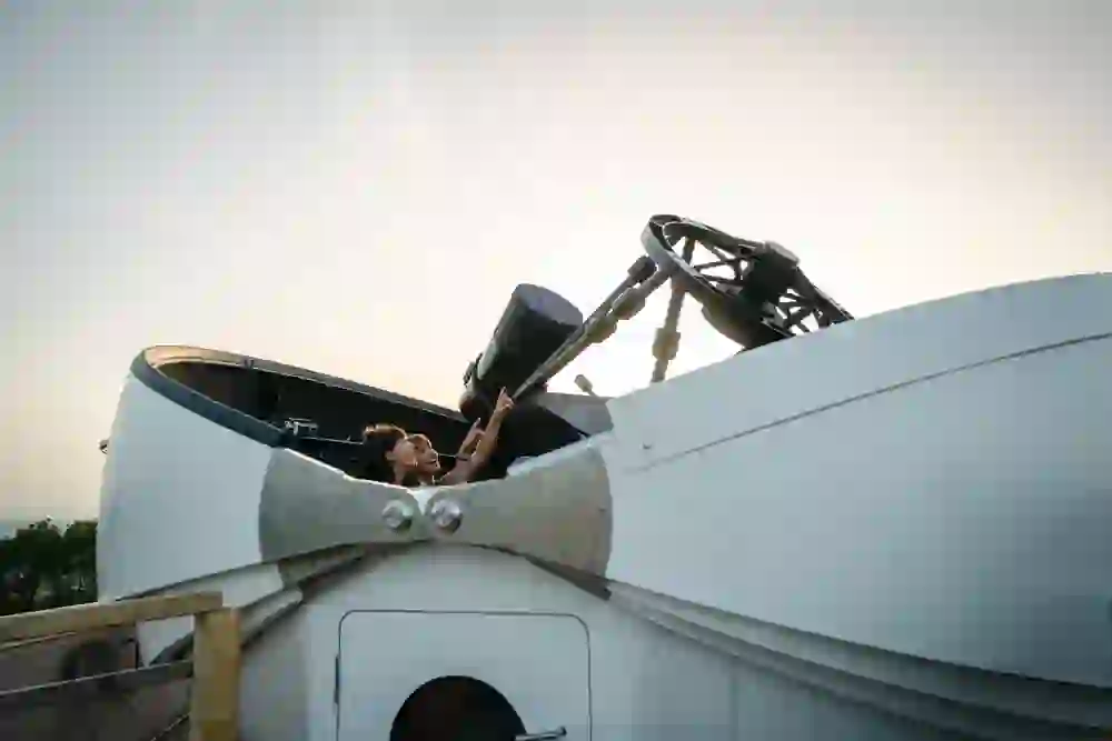 Das Foto zeigt zwei Personen, die bei Dämmerung durch das grosses Teleskop in einer Sternwarte des Space Eye Gantrisch in den Himmel schauen.