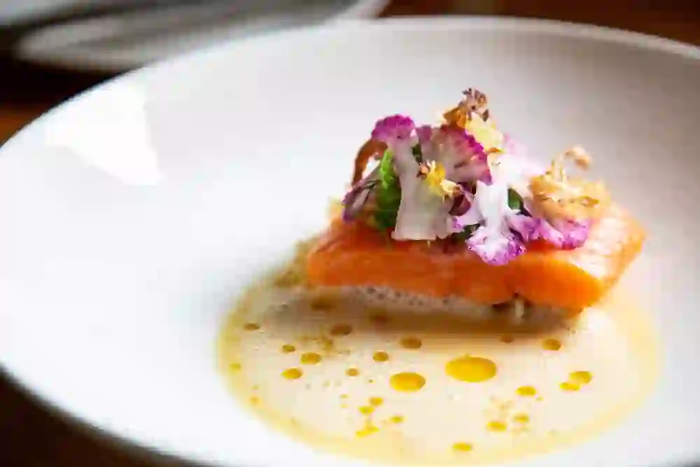 The picture shows an artfully presented dish from the restaurant Zum Äusseren Stand in Bern, in which bright salmon is arranged with delicate flowers and an aromatic sauce to create a gastronomic work of art.