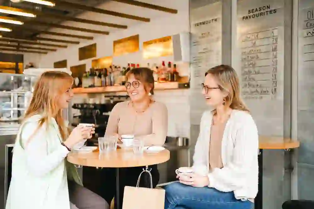 Three friends enjoy lively conversation and coffee at "VERSA Kaffee & Wermut", surrounded by the warm and cheerful atmosphere of the café.