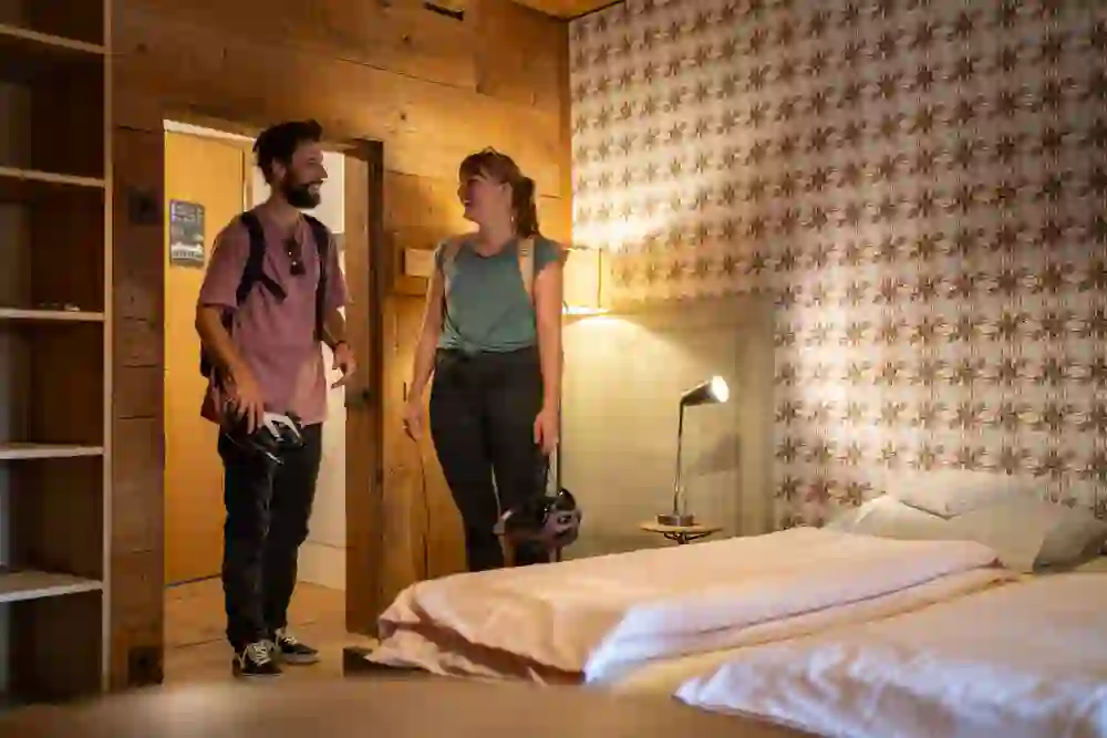 La photo montre une pièce lumineuse et confortable au sein de l'auberge de jeunesse du château de Burgdorf. Deux personnes sont en train de discuter et se sourient, ce qui donne une atmosphère amicale et accueillante.