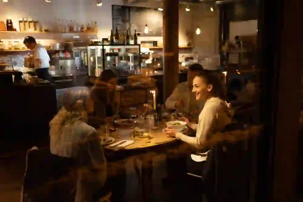 The picture shows a lively and warm atmosphere in a restaurant. Guests sit relaxed while eating and drinking, chatting animatedly. The atmospheric lighting and the busy service in the background give the place an inviting ambience.