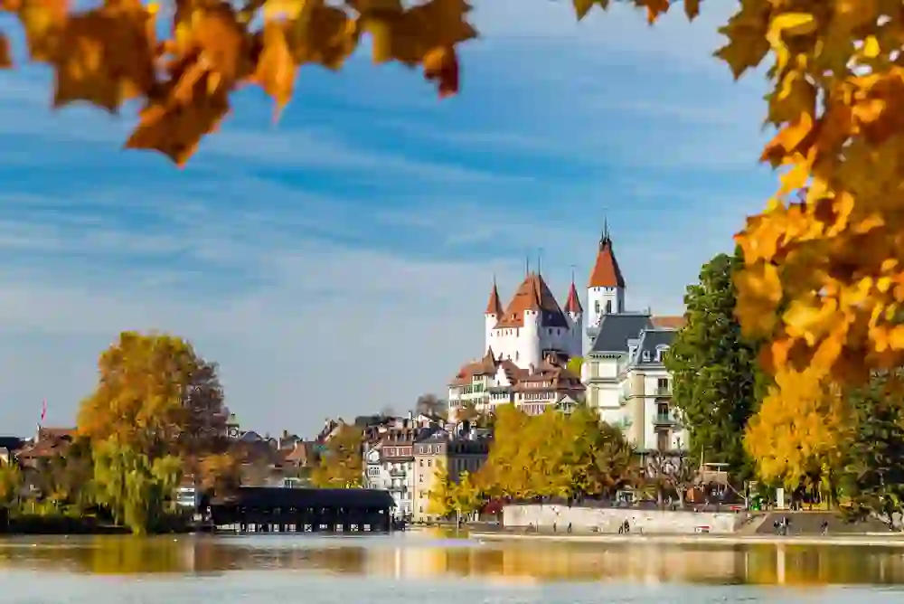 L'immagine mostra il pittoresco Castello di Thun, che si erge maestoso sulle rive di un lago. L'architettura del castello, con le sue caratteristiche torri e il suo colore bianco, si staglia contro il cielo azzurro.