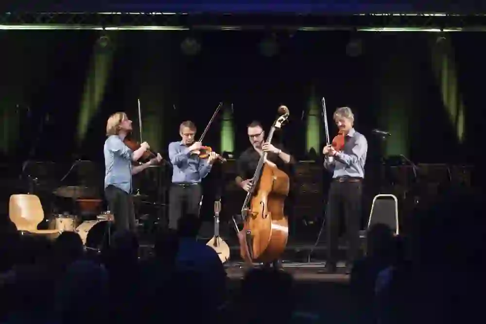 Ein Streichquartett spielt leidenschaftlich auf einer beleuchteten Bühne vor einem Publikum. Die Intensität und Hingabe der Musiker schaffen eine fesselnde, fast greifbare Atmosphäre musikalischer Hingabe