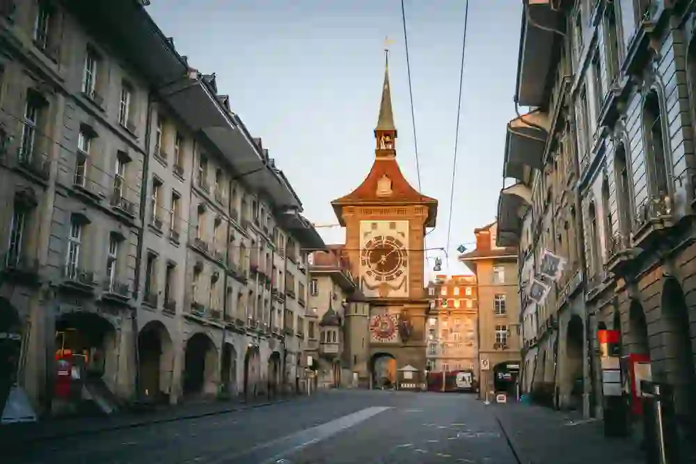 The picture shows a street scene in Bern, Switzerland, with a view of the Zytglogge, a historic clock tower that is a well-known landmark of the city. You can also see tram tracks, traditional buildings and vehicles parked on the roadside.