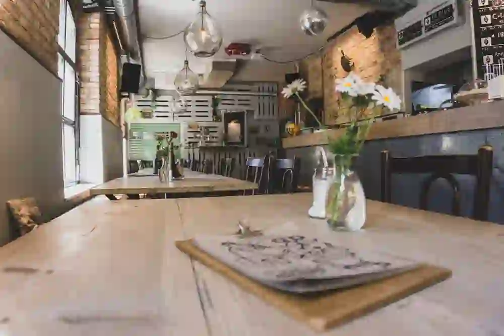 The picture shows the cosy interior of a café with a rustic flair, characterised by brick walls and wooden furniture. The relaxed atmosphere is emphasised by fresh flowers on the tables and soft lighting, ideal for pleasant conversations and relaxed moments.
