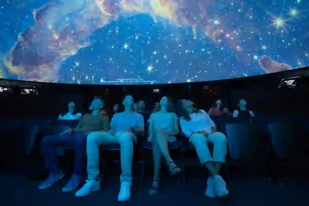 Das Publikum im dunklen Raum des Space Eye Gantrisch wird in den Bann des funkelnden Sternenhimmels gezogen, der sich über sie wölbt. Staunende Blicke richten sich nach oben, auf die leuchtenden Farben der kosmischen Nebel und die klare Strahlkraft der Sterne, während das Gefühl der Unendlichkeit des Universums greifbar wird.