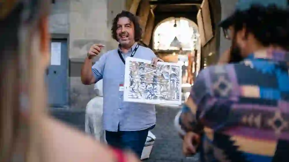 Das Bild zeigt einen Reiseführer, der während einer Stadtführung ein Bild hält und etwas erklärt. Die Tourteilnehmer hören zu. Sie befinden sich bei der Zytglogge (Zeitglogge) in Bern.