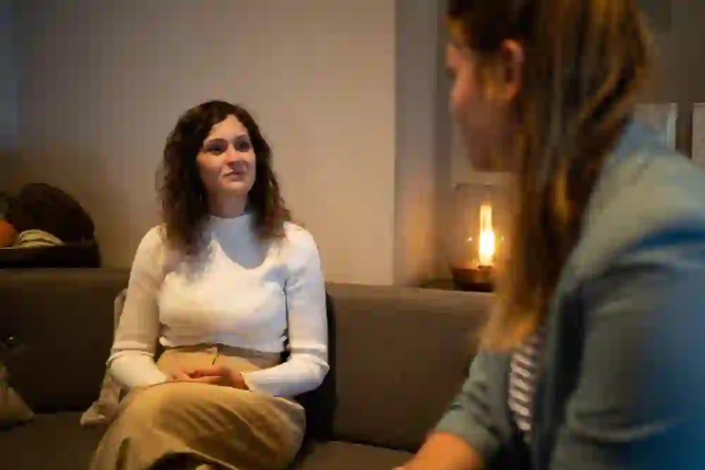 Das Bild zeigt zwei Frauen in einem ruhigen Gespräch in einem gemütlichen Café. Die Person im Vordergrund hört aufmerksam zu, ihr entspannter Ausdruck und die warme Umgebungsbeleuchtung tragen zu einer friedlichen und freundlichen Atmosphäre bei.