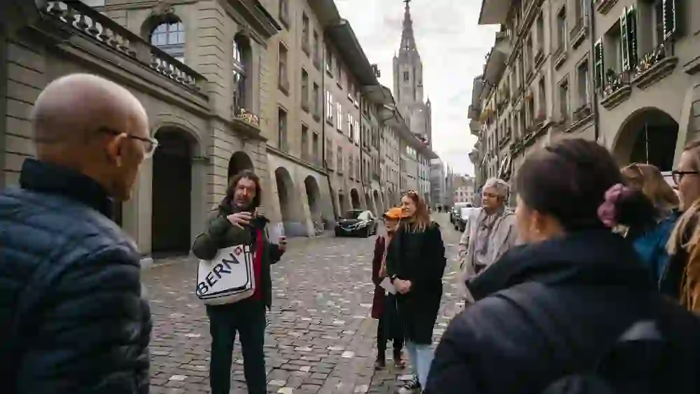 Ein Führer teilt mit einer Gruppe in den historischen Strassen Berns Anekdoten, während im Hintergrund der gotische Turm der Kathedrale emporragt, was der „1848 – Bern wird Bundesstadt“ Tour einen Hauch von Vergangenheit verleiht.