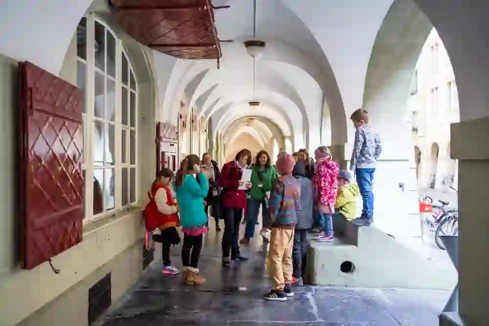 Under Bern's arcades, a group of children discover new things with their city guide. Their eyes are curiously directed upwards and the relaxed atmosphere invites them to learn through play.