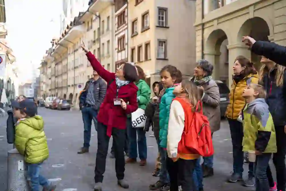 A group of children eagerly follow the pointing gestures of their guide on a children's city tour in Bern. Their upturned faces reflect amazement and the pleasure that a sunny day brings for little explorers.