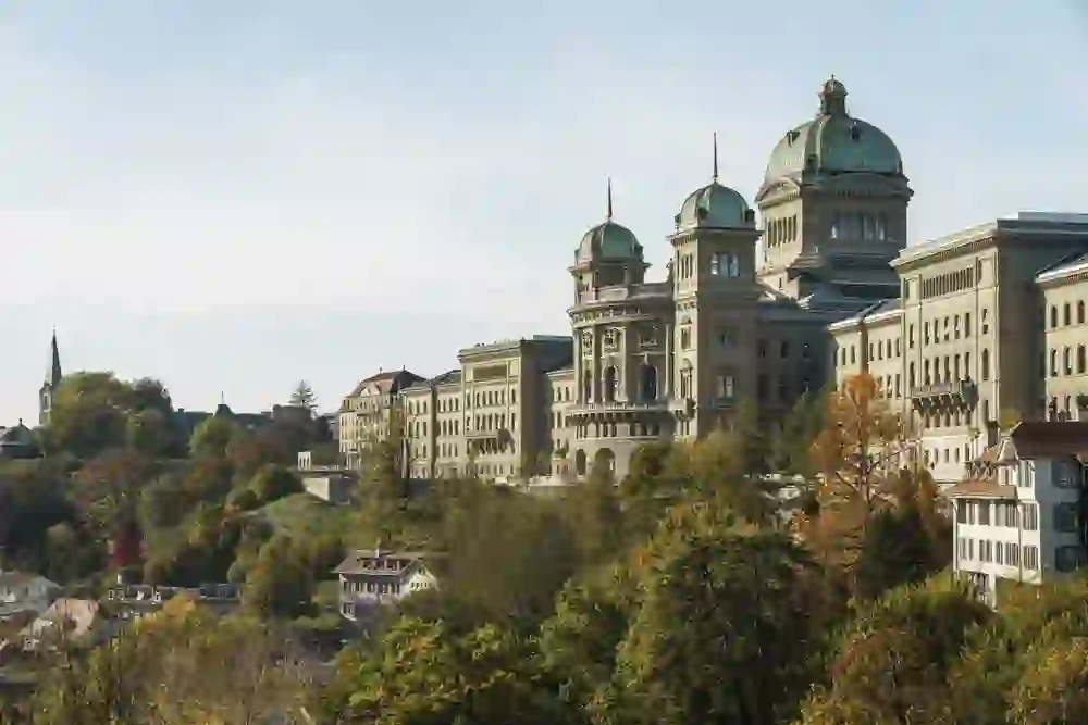 Das Bild fängt das Bundeshaus in Bern ein, eingebettet in die herbstliche Farbpracht der Bäume und bietet einen Eindruck von Erhabenheit und historischer Bedeutung in einem lebendigen städtischen Raum.