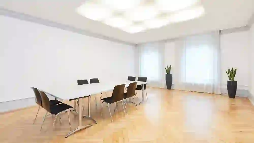 Das Bild zeigt einen hellen, geräumigen Konferenzraum im Kongresszentrum Kreuz Bern. Saubere Linien und eine minimalistische Einrichtung vermitteln eine Atmosphäre der Klarheit und Professionalität. Natürliches Licht flutet durch die Fenster, unterstützt von sanftem, künstlichem Licht von oben, was Ruhe und Fokus für bevorstehende Diskussionen bietet. Die Pflanzen am Rand fügen einen Hauch von Leben und Energie hinzu.